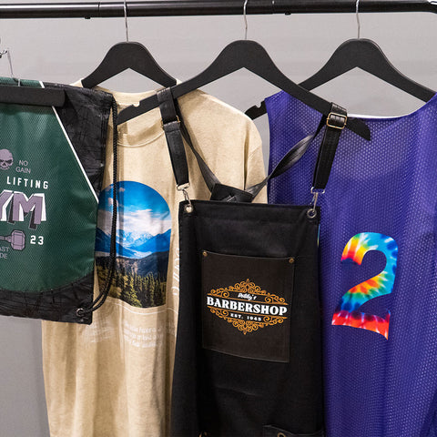 Drawstring Bag, T-Shirt, Apron, and a Jersey hanging on a rack with DTF Transfers applied to them